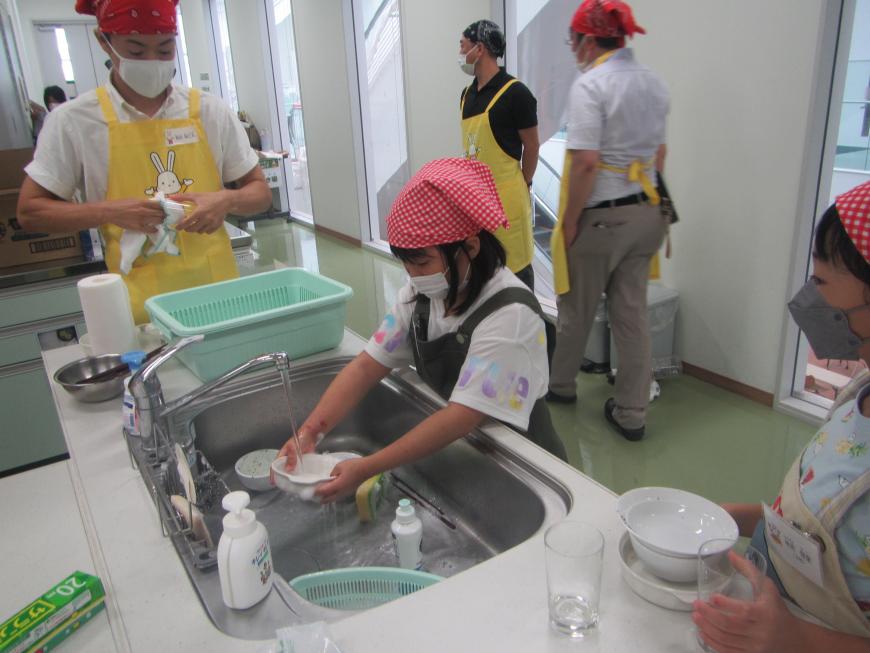 調理職員が見守る中、女の子が食器を洗っている写真