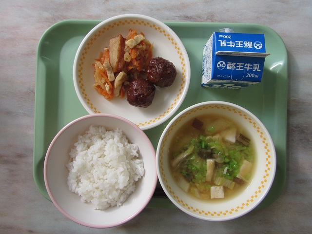 若草色のトレーの上に、ごはん、みそ汁、甘酢肉だんごとひき菜炒り盛り付けられた皿、パックの牛乳が乗っている写真