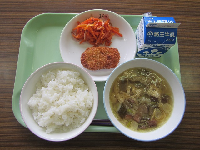 若草色のトレーの上に、ごはん、みそ汁、メンチカツといか人参が盛り付けられた皿、パックの牛乳が乗っている写真