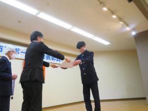 制服姿の男子生徒と市長が向かい合って立っている表彰式の様子の写真