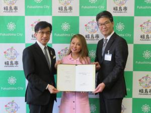 ピンク色の服を着たボーク重子さんを中央に市長と関係者の男性が横一列に並んでいる写真