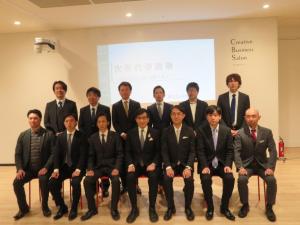白い壁に資料が映し出された前に設置された椅子に市長を含めて7人が座り、後列に6人が並んでいる記念写真