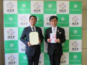 バックパネルの前で勅使河原取締役と目録を持った市長が並んでいる写真