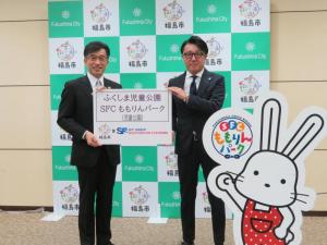 バックパネルの前で「ふくしま児童公園SFCももりんパーク」と書かれたボードを市長と関係者の男性が持っている写真