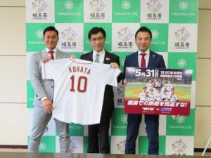 バックパネルの前で、銀次さんと市長で市長のネーム入りの楽天ユニフォームをひろげ、森井社長が試合開催のボードを持っている写真