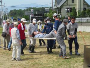 広場で救急隊員が寄り添って、男性4名が担架で人を運んでいる写真