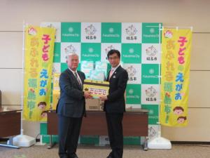 バックパネルの両脇に、幟が立っている前で市長と男性で大きな駐車券のレプリカを持っている写真