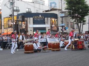 多くの観客が見ている中、法被を着た人たちが太鼓をたたいている写真