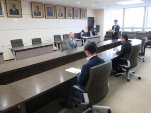 長机に対面で座っている男性3名が資料を見ながら話をしている写真