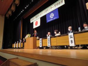 定期総会の横断幕が吊り下げられたステージ上に来賓の方が横一列に座っている中で市長が演台に立って話をしている写真