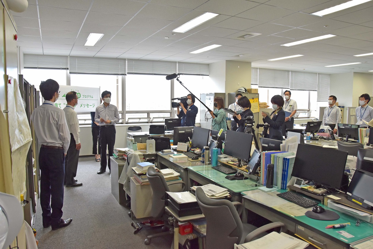 デスクやパソコンが置かれたオフィス内で市長が取材をうけている様子の写真