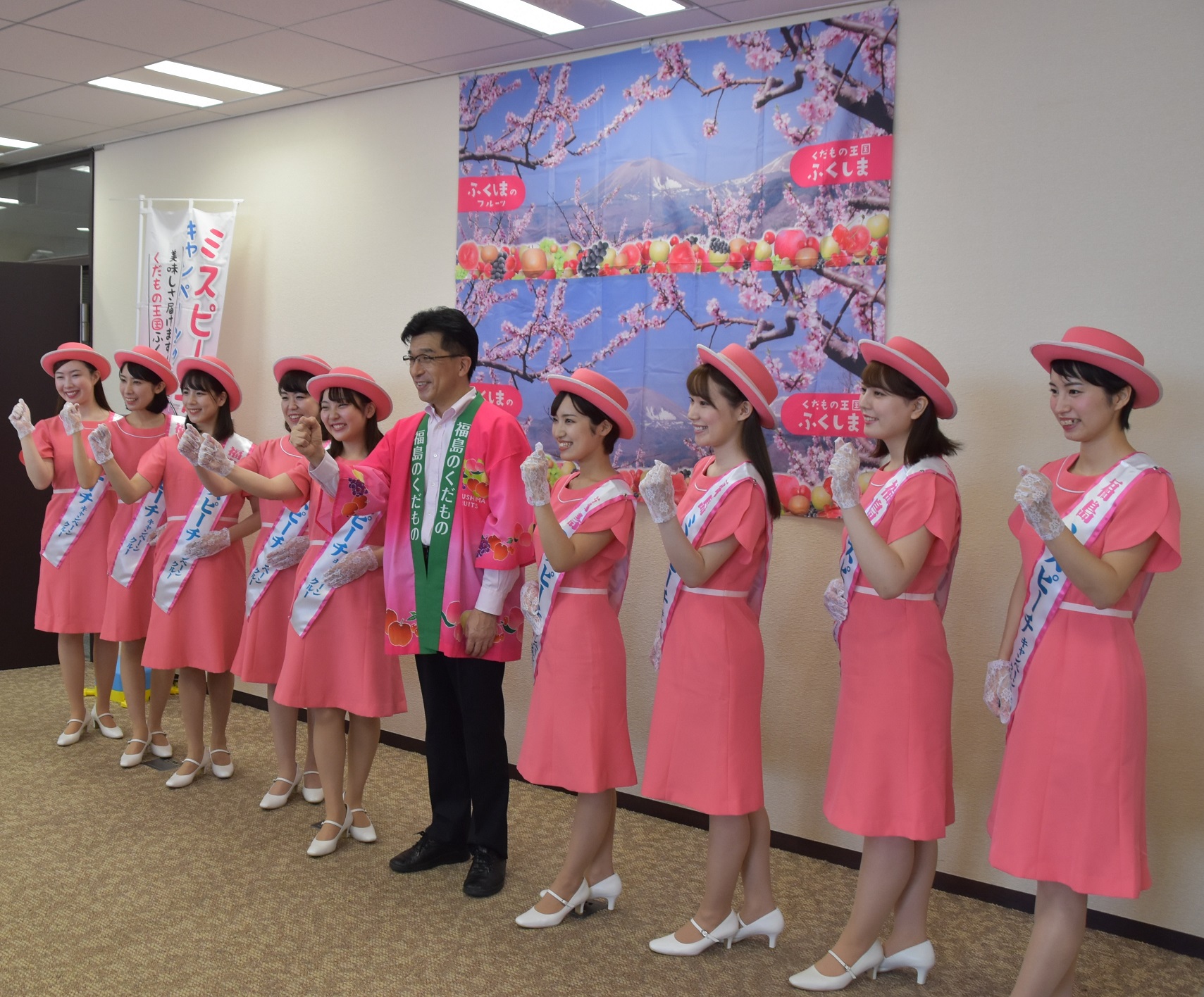 中央にピンクの半被をきた市長がおり、両隣りにピンクのワンピースにピンクの帽子をかぶった女性達が立ちガッツポーズをして記念撮影している写真