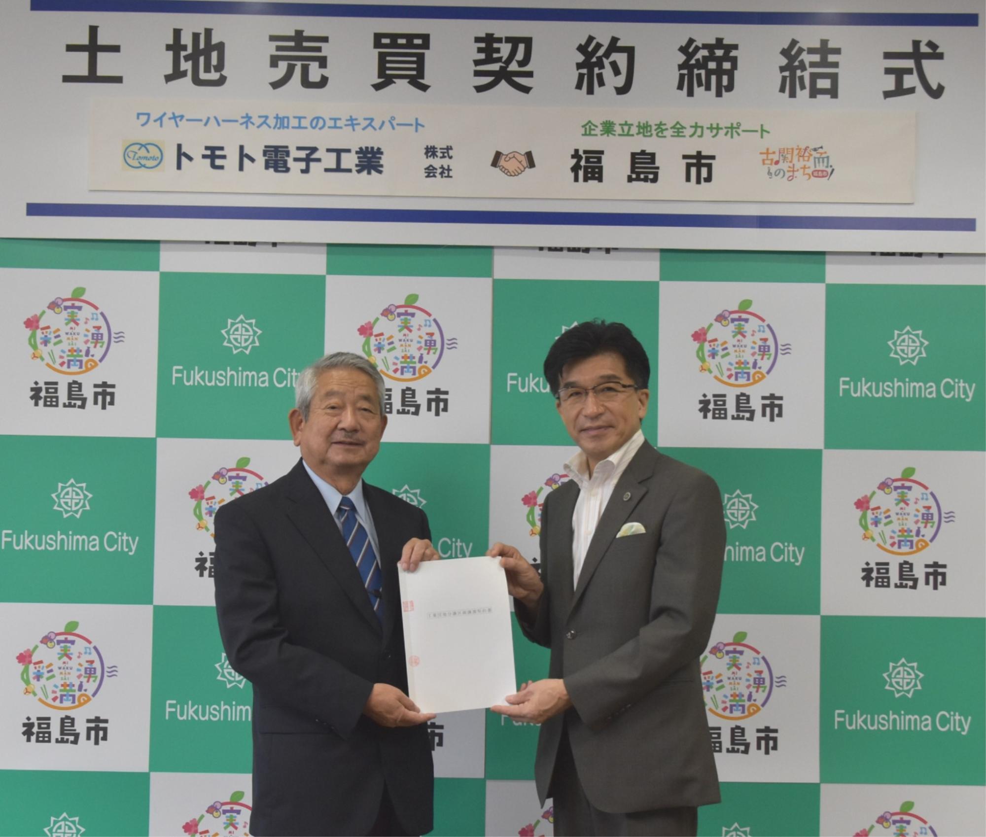 「土地売買契約締結式」と書かれた横断幕と福島市のバックボードの前で市長と男性が契約書を一緒に持ち、記念撮影している写真