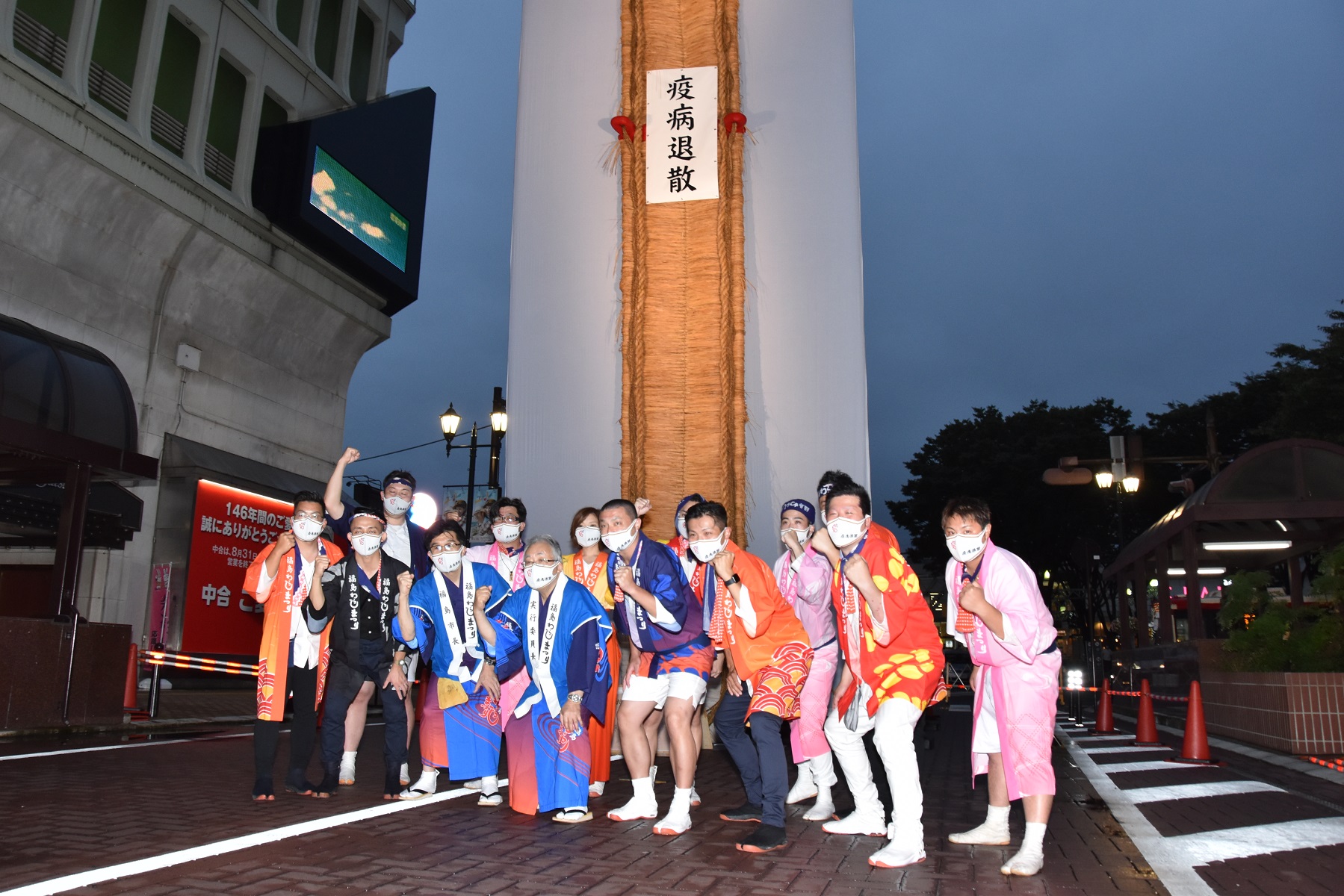 疫病退散と書かれた大きなわらじの前でポーズを決めて撮影する役員と参加者たちの写真