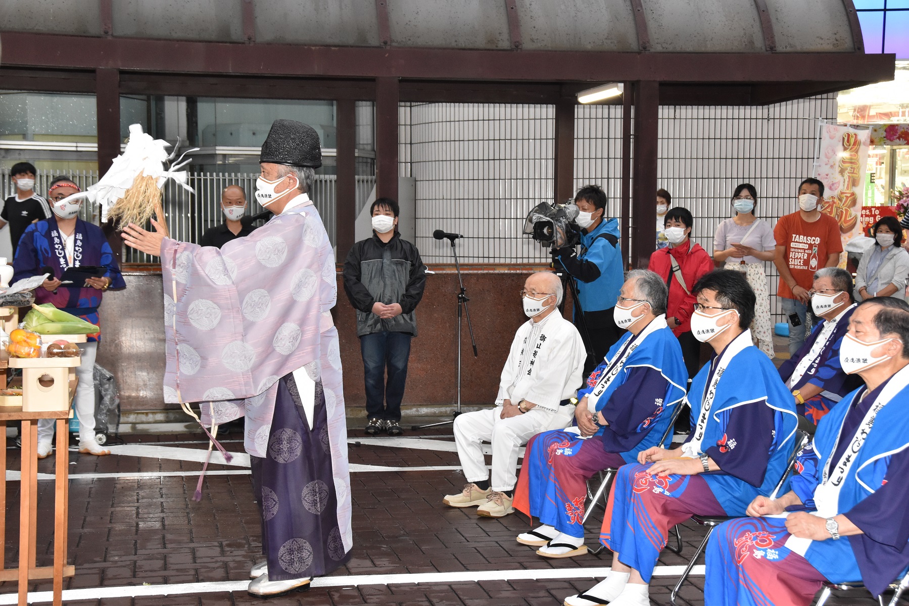 祈願神事を行う神職の後ろで椅子に座り真剣な目で見守る役員を撮影している写真