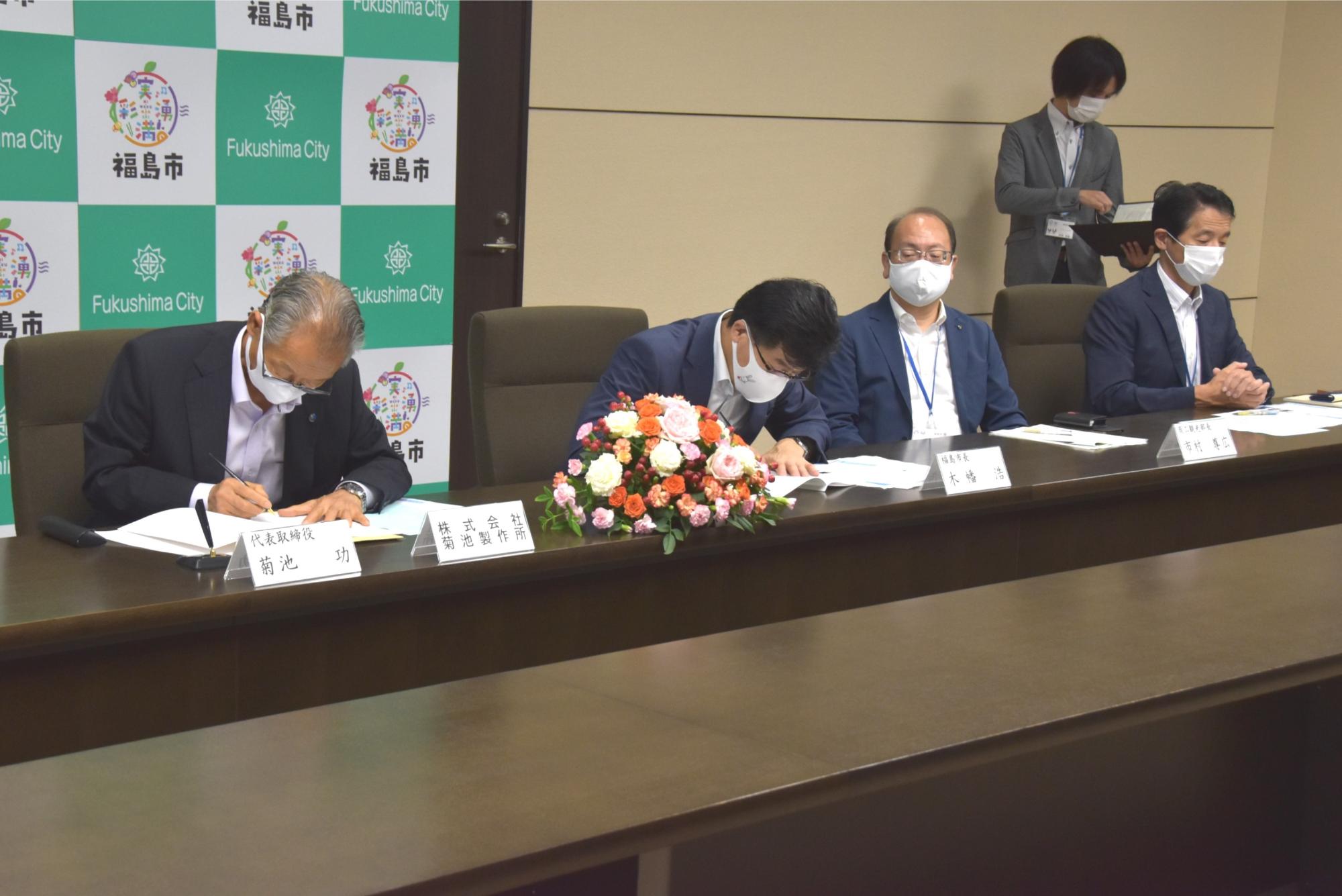 4人の男性が椅子に座り机に置かれた書類を目を通している様子を撮影した写真