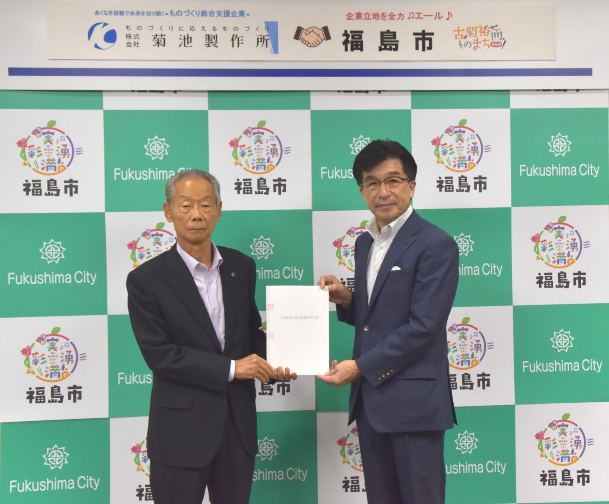 菊池製作所の役員と市長が締結した書類を持ち福島市のロゴが入ったパーテーションの前で撮影している写真