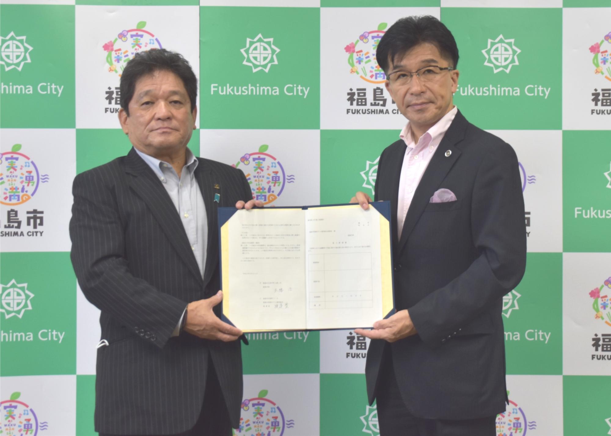 市長応接室で福島市旅館ホテル協同組合の男性と市長が締結した書類を二人で持ち撮影している写真