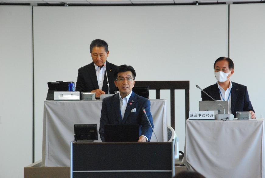議長と事務局長が見ている前で、市長が演台で話をしている写真