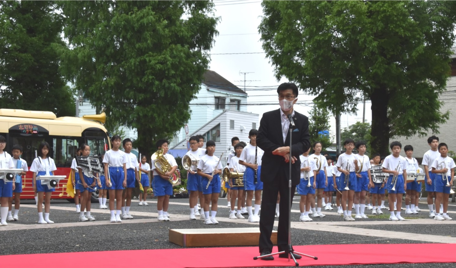 市長がレッドカーペットの上でマイクに向かって話をしており、後ろには福島第三小学校の生徒たちが楽器を手に持ち整列をしている写真