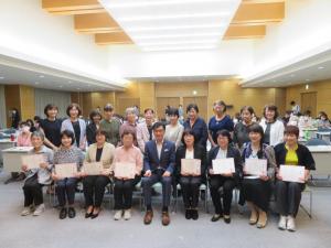 委託状を持った「こんにちは赤ちゃん応援隊」の女性19名と市長が記念撮影した写真
