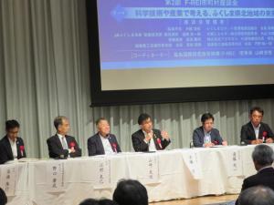 白い幕に名札がつけられた席の中央で市長が説明をしている座談会での写真