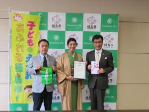 子どものえがおあふれる福島市とかかれた旗の横で男性、着物姿の女性、市長が並んで記念撮影をしている写真