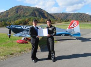 飛行機の前で市長と男性が協定書を持ちながら記念撮影をしている写真