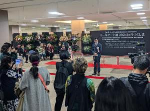ドールアート展in うつくしまの案内板の前でたくさんの来場者に挨拶をしている市長の写真
