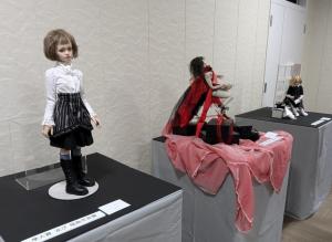 白と黒の服を着た人形、ピンクの布の上に飾られた人形などさまざまな人形が展示されている写真