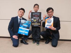 男の子を真ん中に男性が2名両隣にひざまつき3枚のポスターを持ってガッツポーズをしている写真