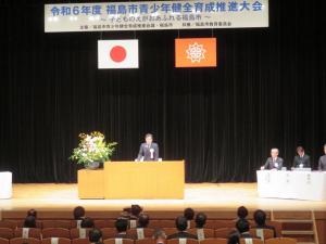 令和6年度福島市青少年健全育成推進大会の幕が飾られた舞台の演台で挨拶をする市長を正面から写した写真