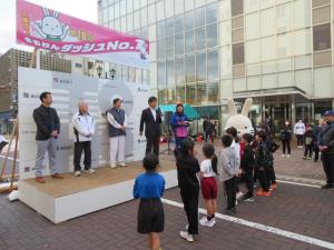 小さな舞台の上で5名の方が並び、その前で子供たちが並んでいるオープニングの写真