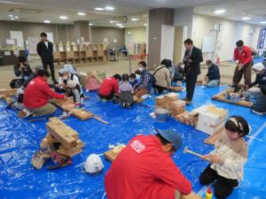 ブルーシートの上で職人さんが参加者の人達と各ブースでものつくりをしている様子を写した写真