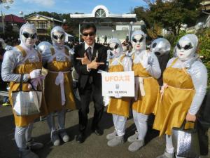 黒いサングラスをかけた男性を中心に宇宙人の格好をし、黒いサングラス姿の参加者の人たちが一緒に記念撮影をしている写真