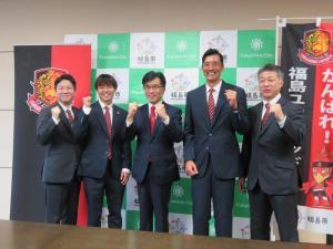バックパネルの前で、市長を中央に福島ユナイテッドFCの選手や関係者の4人が並びガッツポーズをしている写真