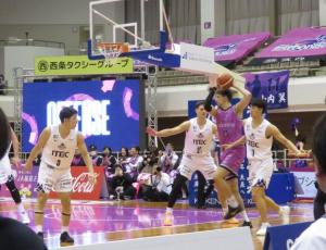白いユニフォームの相手チームがゴール付近でディフェンスを固める中、ピンク色のユニフォームを着た福島ファイヤーボンズの選手が、両手でボールを構えながら左足を上げ、シュート体勢に入ろうとしているゲームの一瞬を捉えた写真