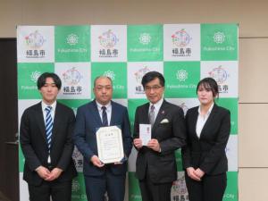 バックパネルの前で、OKIシンフォテック労働組合の3名と目録を持った市長が横一列に並んでいる記念写真