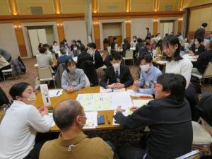 グループごとに分かれて座った参加者たちが話し合っているワークショップの様子の写真