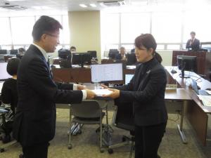 長机の席に一人ずつモニターが設置された庁議室で、女性と市長が向かい合って立っている写真