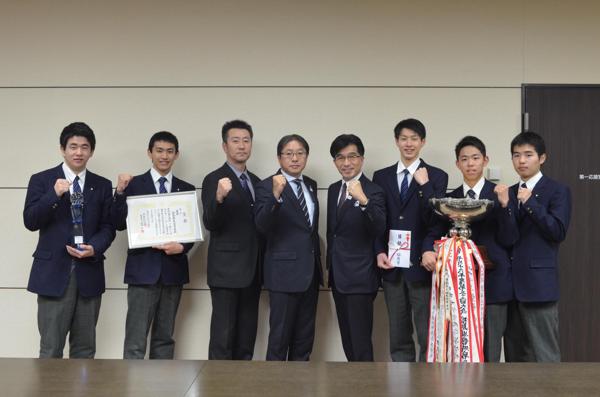 優勝カップや賞状を手に持った制服姿の福島県立福島商業高等学校男子バレーボール部の皆さんと市長が、ガッツポーズを取っている写真