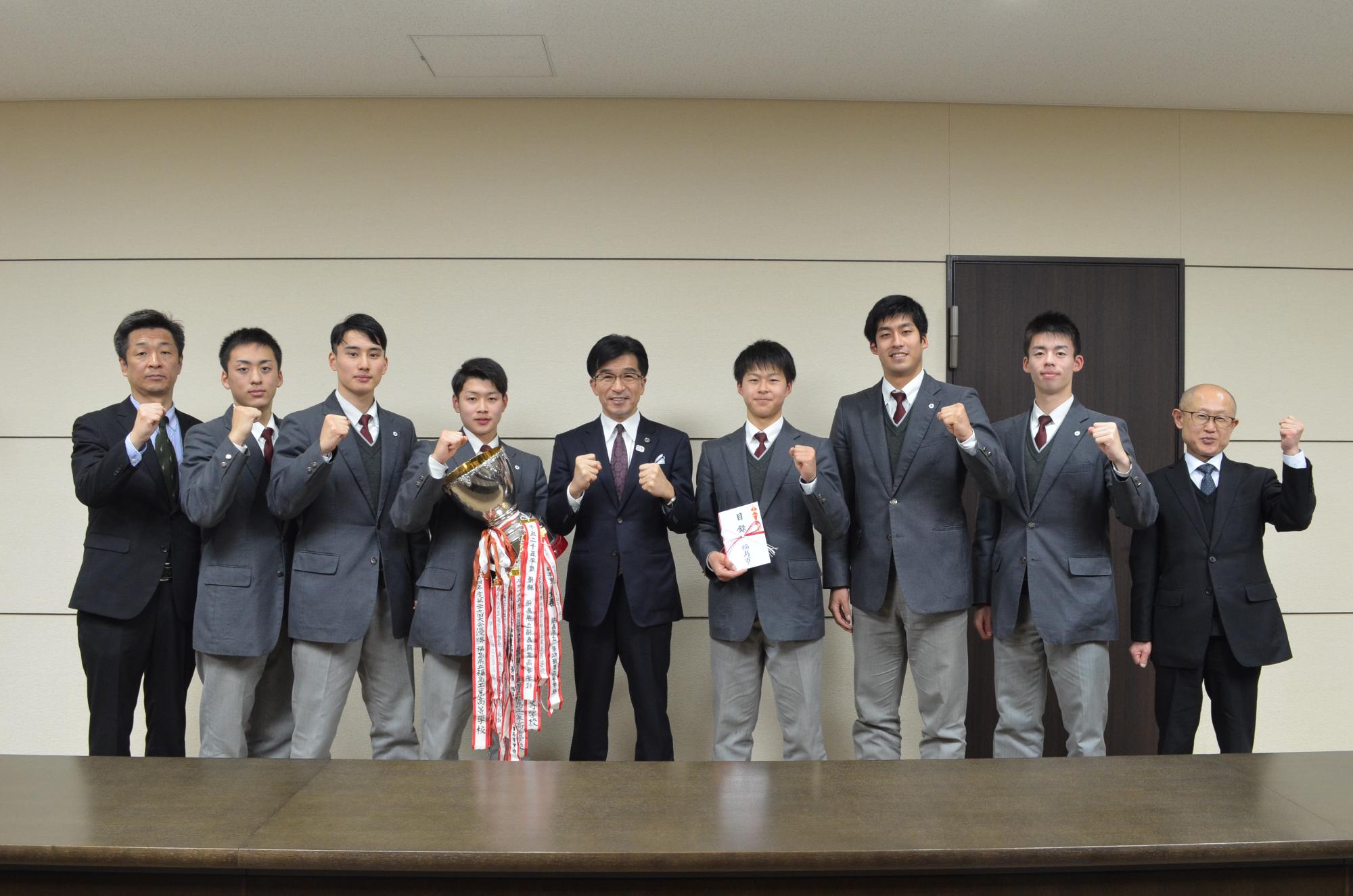 優勝カップを手に持った福島県立福島南高等学校男子バスケットボール部の皆さんと市長がガッツポーズを取っている写真