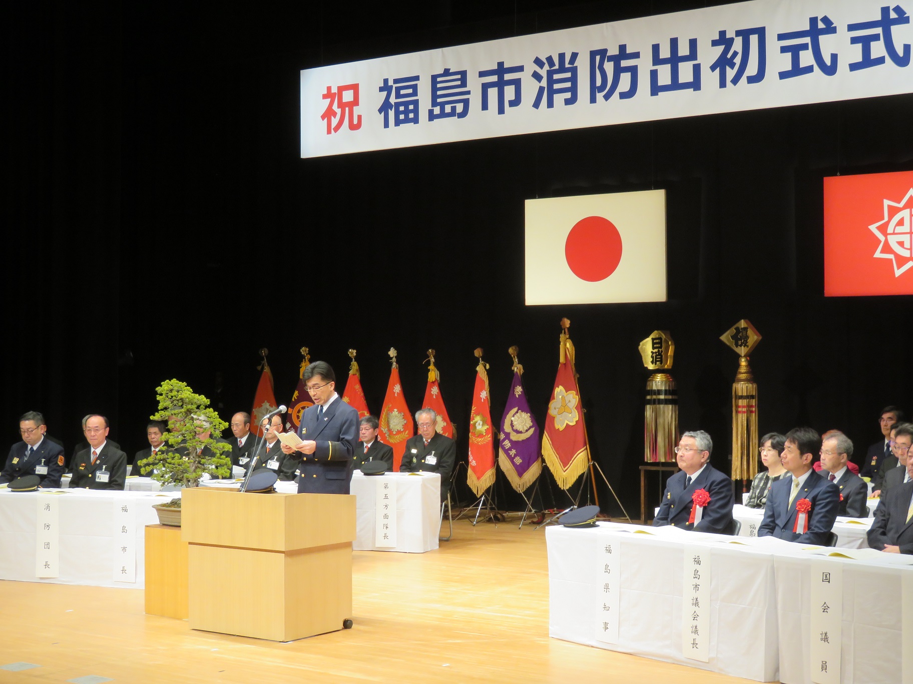 ステージに関係者が来賓席に座っており、演壇で市長が話をしている写真