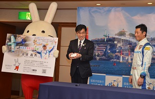 ももりんが拡大された室屋義秀さんの名刺パネルを手に持ち、その横で名刺を手に持つ市長と、室屋義秀さんが並んでいる写真