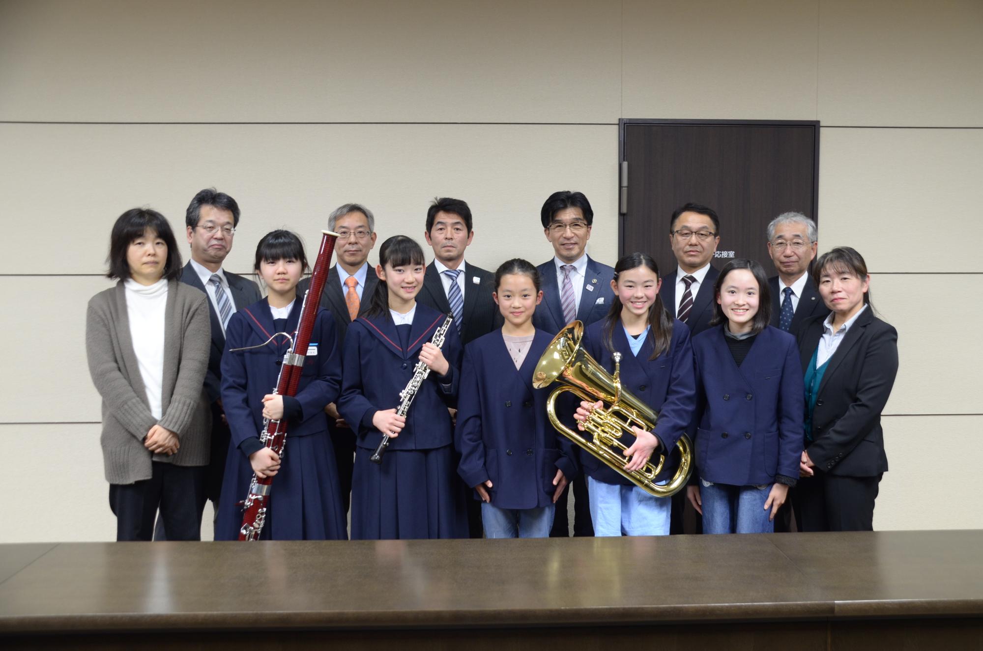 小中学校音楽クラブの皆さんが楽器を手に持ち、市長とNTTドコモグループの関係者と並んでいる写真