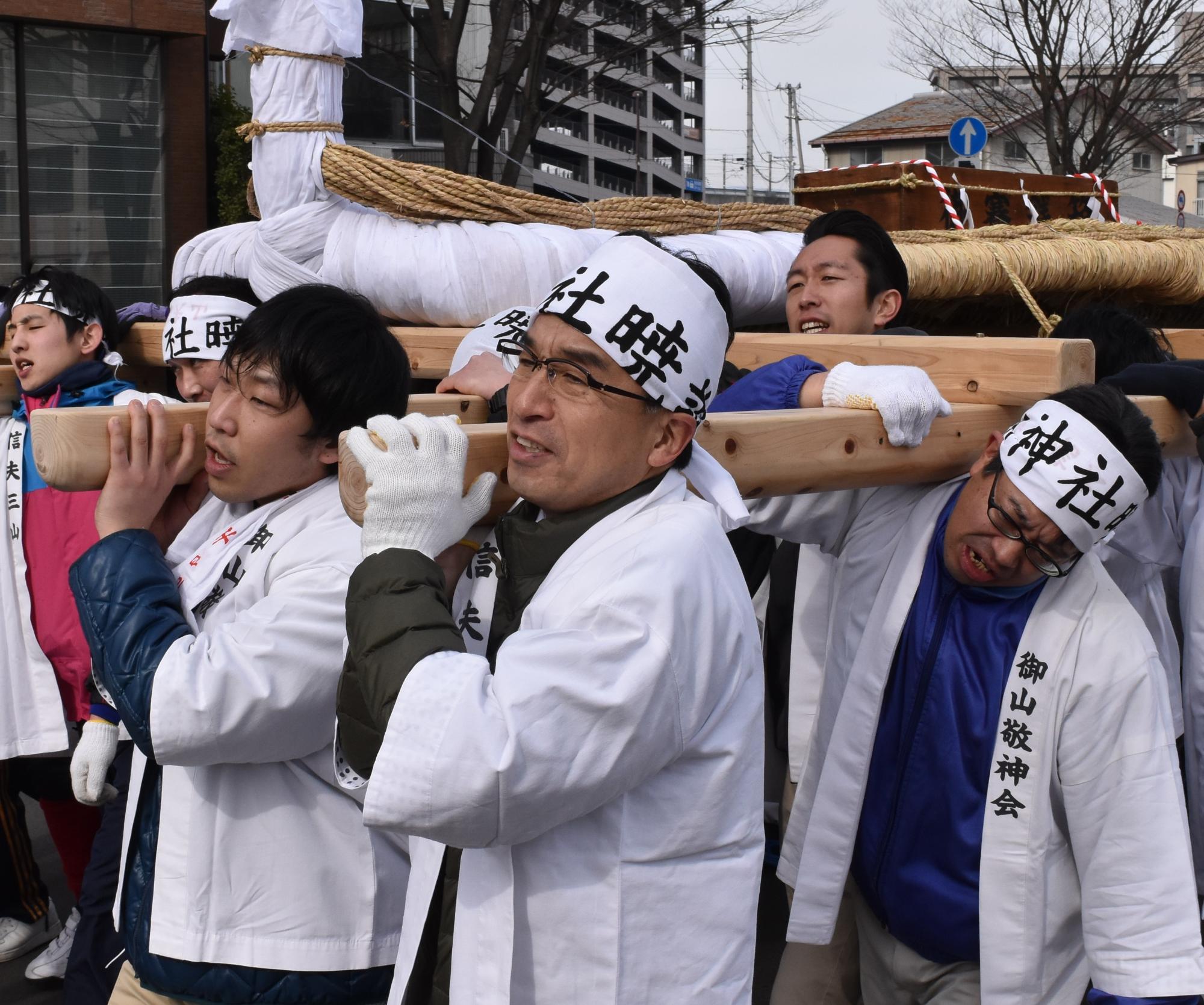 白のはっぴを着た男性達が、大きな日本一のわらじを肩に担いで、市内を練り歩いている写真