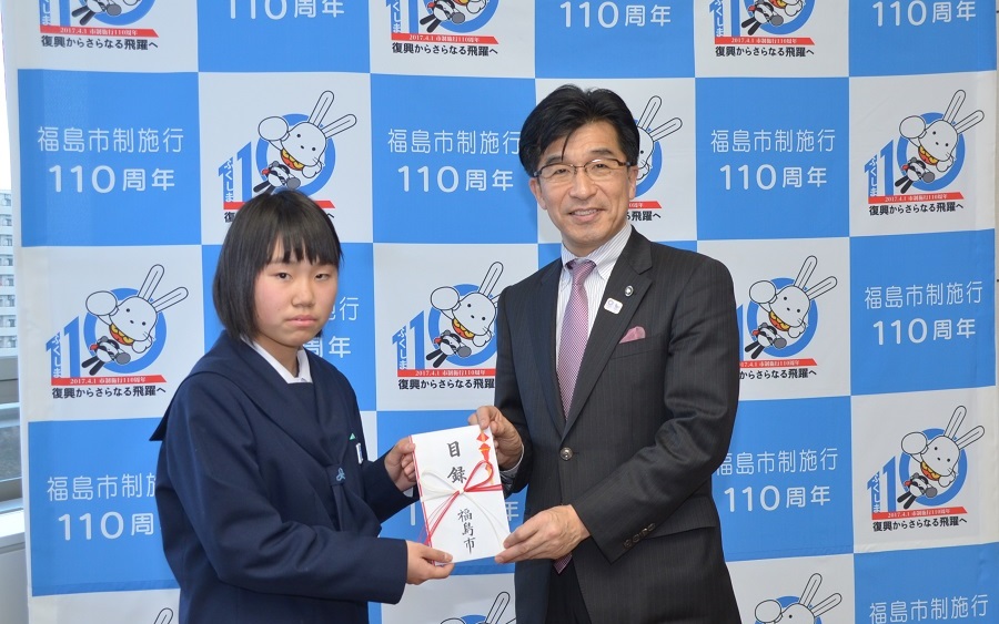 バックパネルの前で女子中学生に目録を手渡す市長の写真