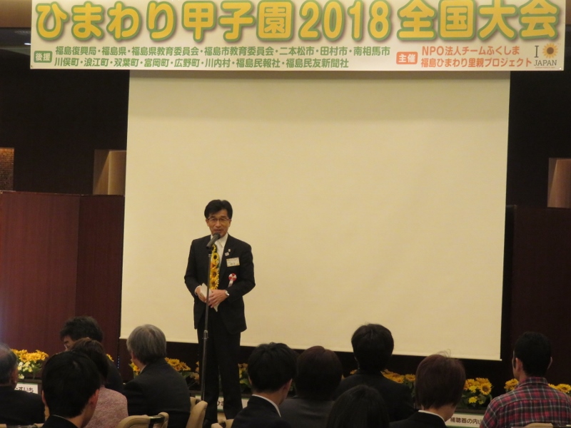 「ひまわり甲子園2018全国大会」のパネルの下、市長が参加者に向けて話をしている写真