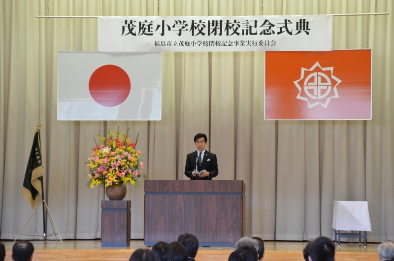 「茂庭小学校閉校記念式典」の吊り看板があり、演壇で話をする市長の写真