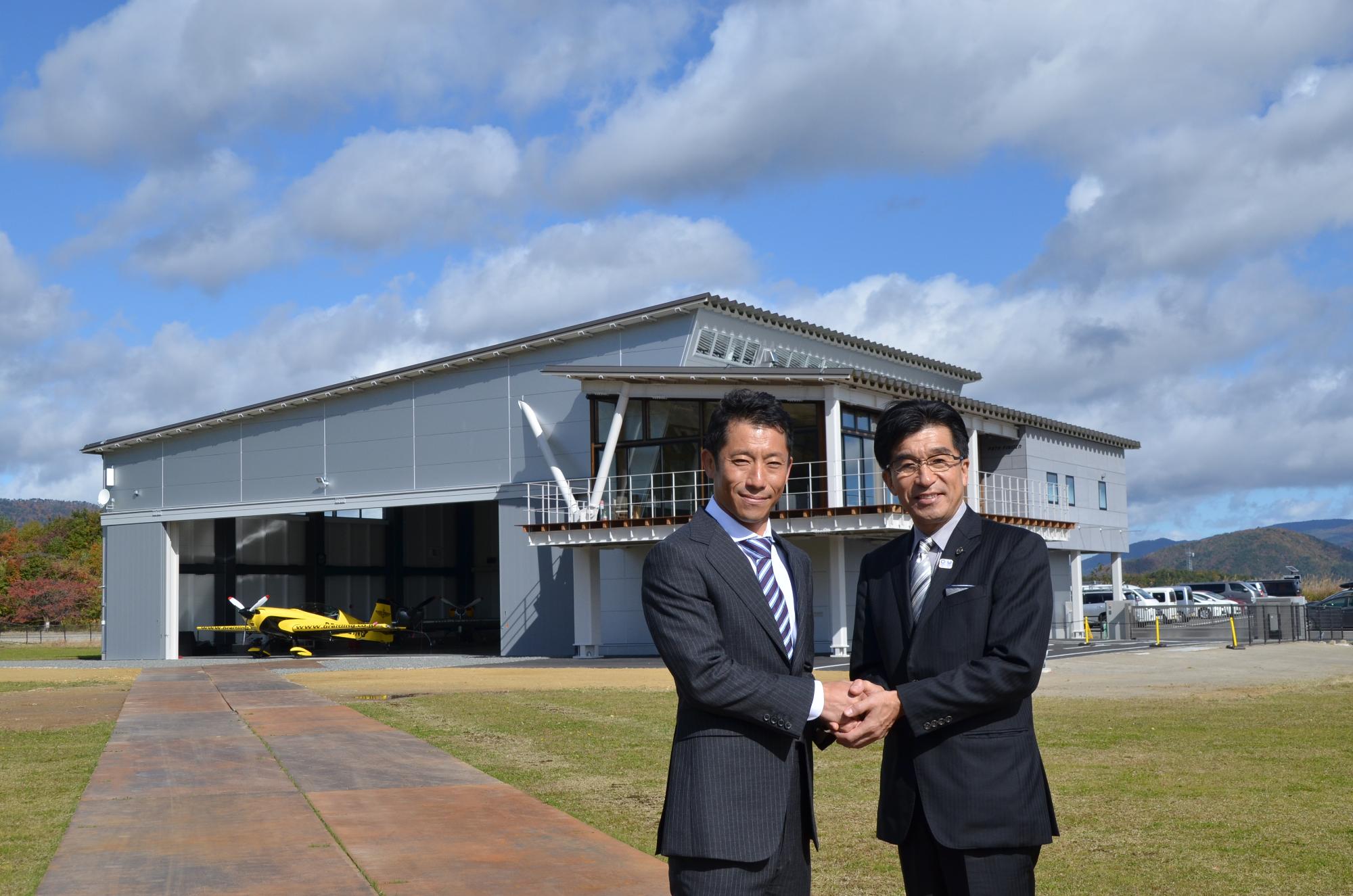 航空機展示場の建物前で、市長とむろやさんが握手を交わしている写真